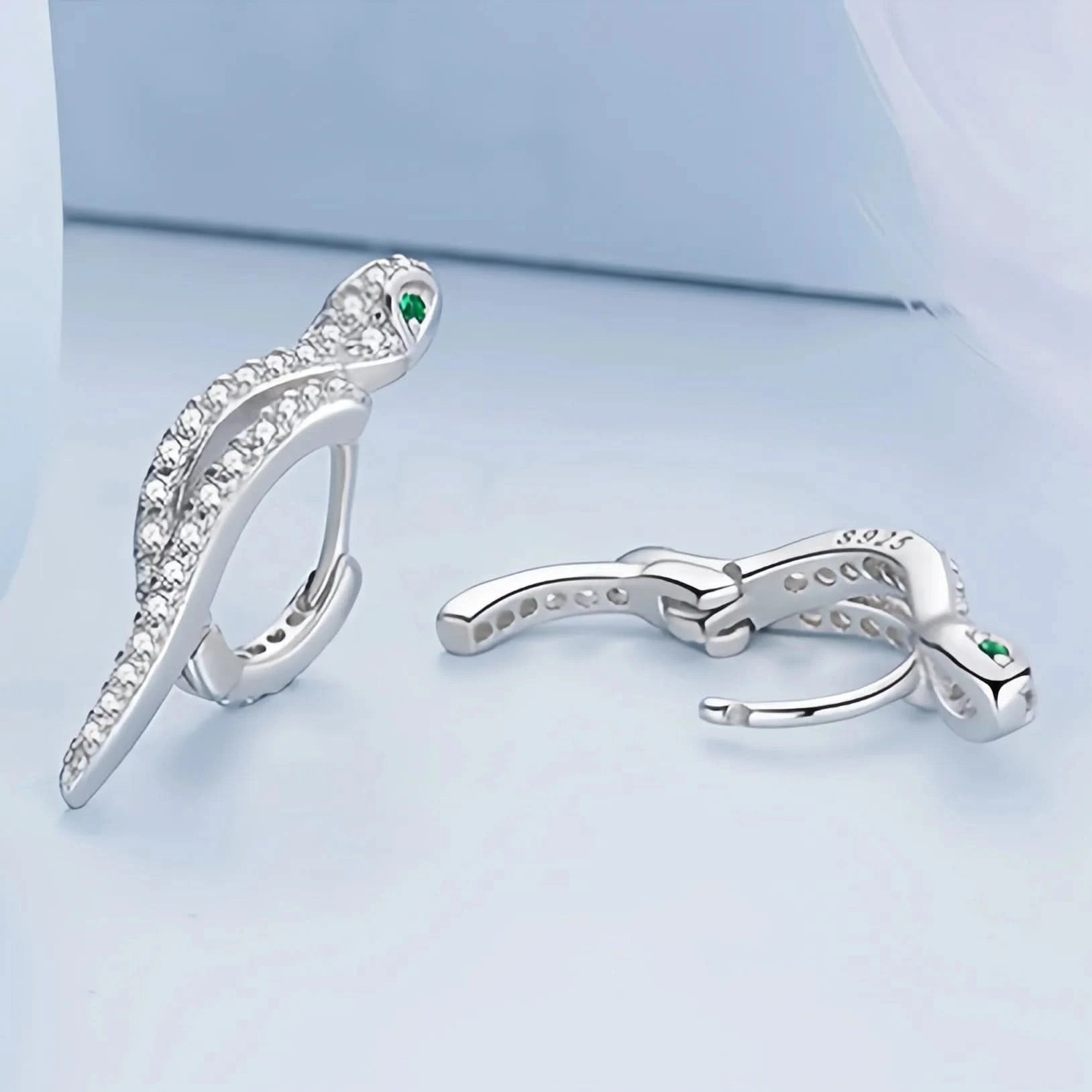 An elegant silver ring designed to resemble a serpent, adorned with numerous small crystals along its body. The snake's head is detailed with a pair of green crystal eyes, and the ring is stamped with 'S925' to indicate sterling silver purity.