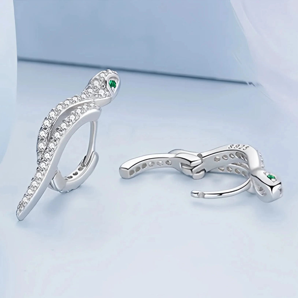 An elegant silver ring designed to resemble a serpent, adorned with numerous small crystals along its body. The snake's head is detailed with a pair of green crystal eyes, and the ring is stamped with 'S925' to indicate sterling silver purity.