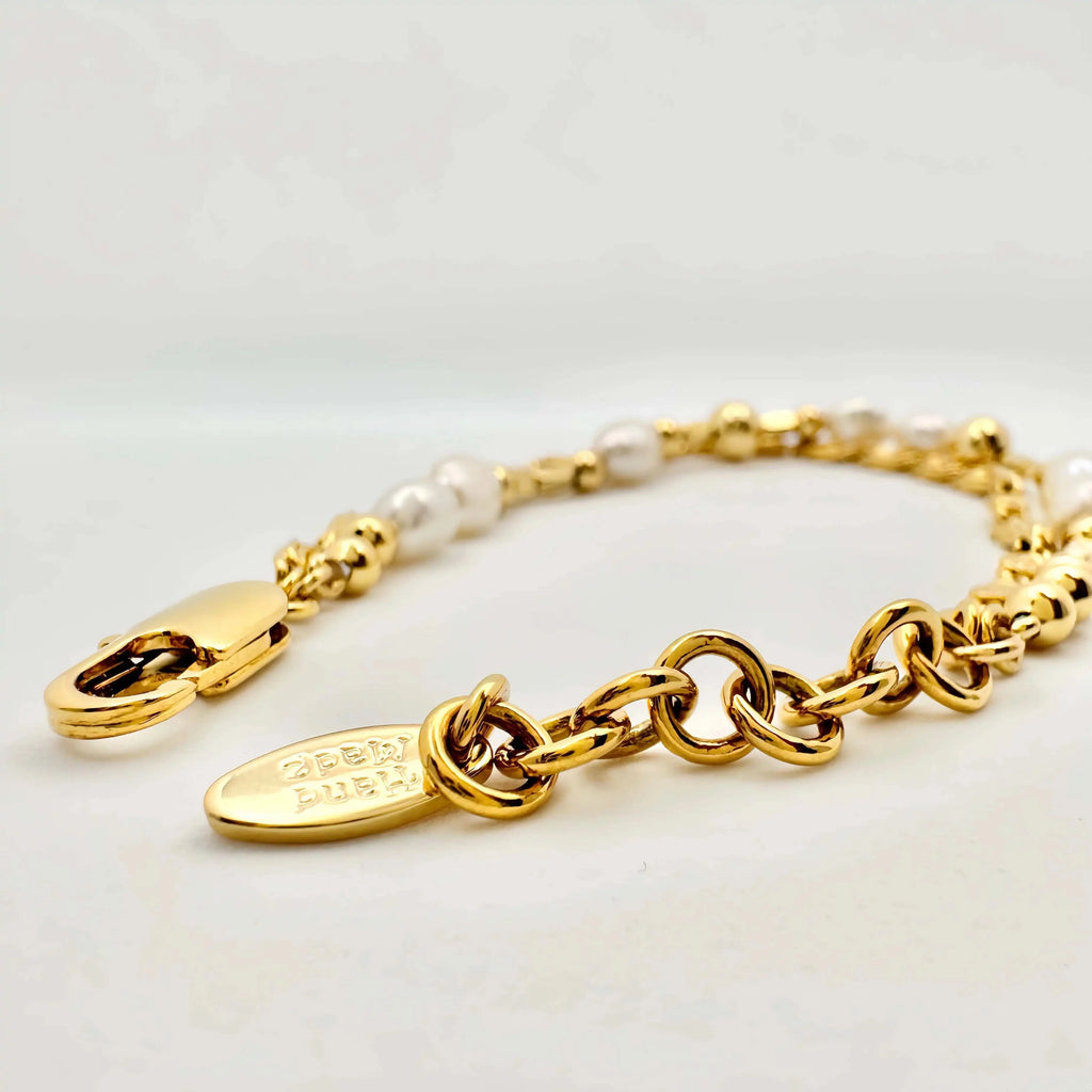 A golden bracelet elegantly composed of alternating white pearls and polished gold spheres, creating a harmonious blend of texture and shine. The bracelet features a clasp with intricate detailing, and it's displayed against a neutral background, highlighting its luxurious appeal.
