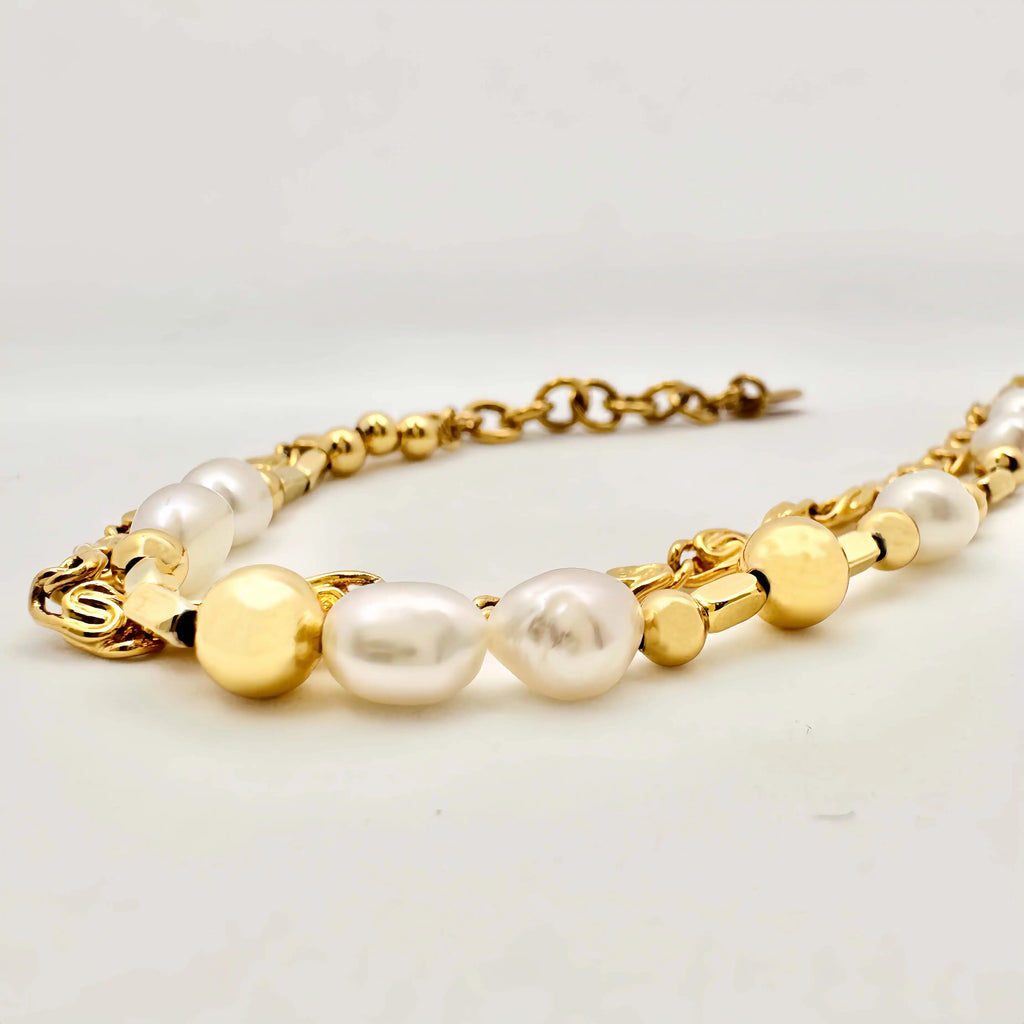 A golden bracelet elegantly composed of alternating white pearls and polished gold spheres, creating a harmonious blend of texture and shine. The bracelet features a clasp with intricate detailing, and it's displayed against a neutral background, highlighting its luxurious appeal.