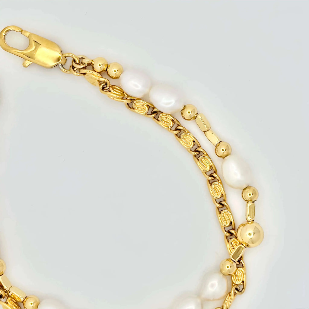 A golden bracelet elegantly composed of alternating white pearls and polished gold spheres, creating a harmonious blend of texture and shine. The bracelet features a clasp with intricate detailing, and it's displayed against a neutral background, highlighting its luxurious appeal.