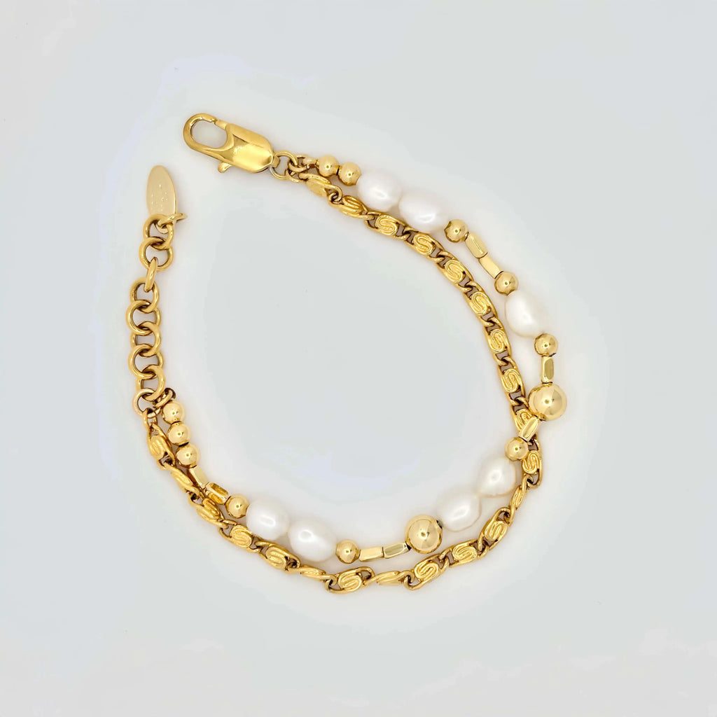A golden bracelet elegantly composed of alternating white pearls and polished gold spheres, creating a harmonious blend of texture and shine. The bracelet features a clasp with intricate detailing, and it's displayed against a neutral background, highlighting its luxurious appeal.