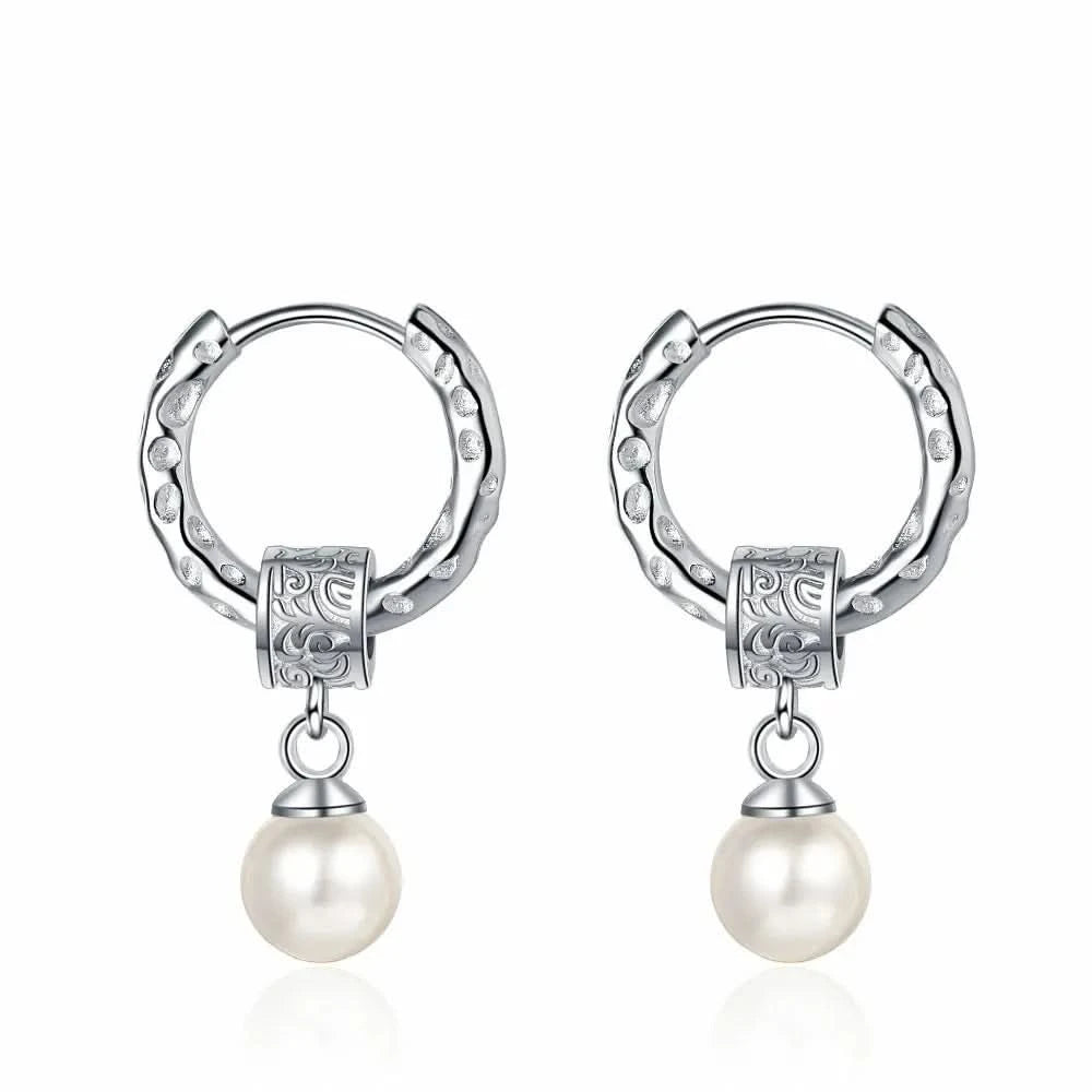 A pair of silver earrings displayed on a white background. Each earring features a textured hoop with an organic, molten-like design, attached to a decorative square bead with intricate patterns. A classic white pearl dangles elegantly from the bead, adding a touch of timeless elegance to the modern design.