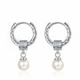 A pair of silver earrings displayed on a white background. Each earring features a textured hoop with an organic, molten-like design, attached to a decorative square bead with intricate patterns. A classic white pearl dangles elegantly from the bead, adding a touch of timeless elegance to the modern design.