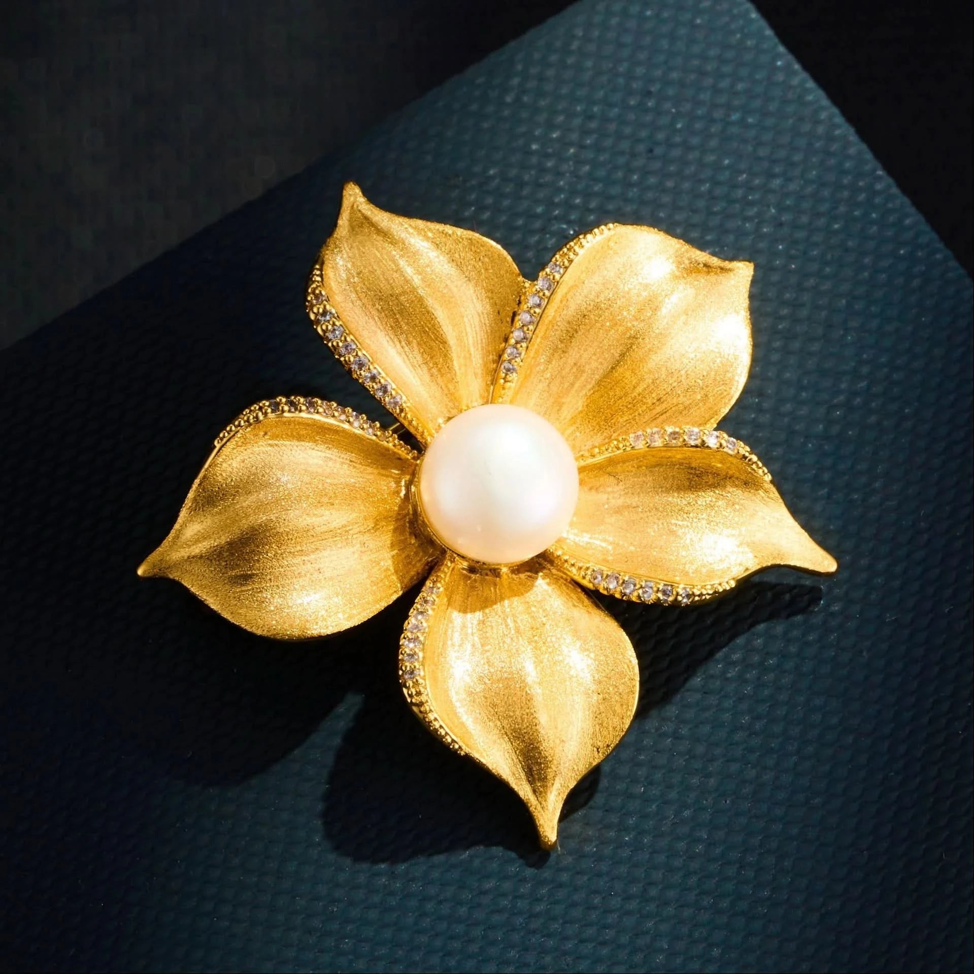 Close-up of brushed gold flower brooch with freshwater pearl and cubic zirconia edged petals