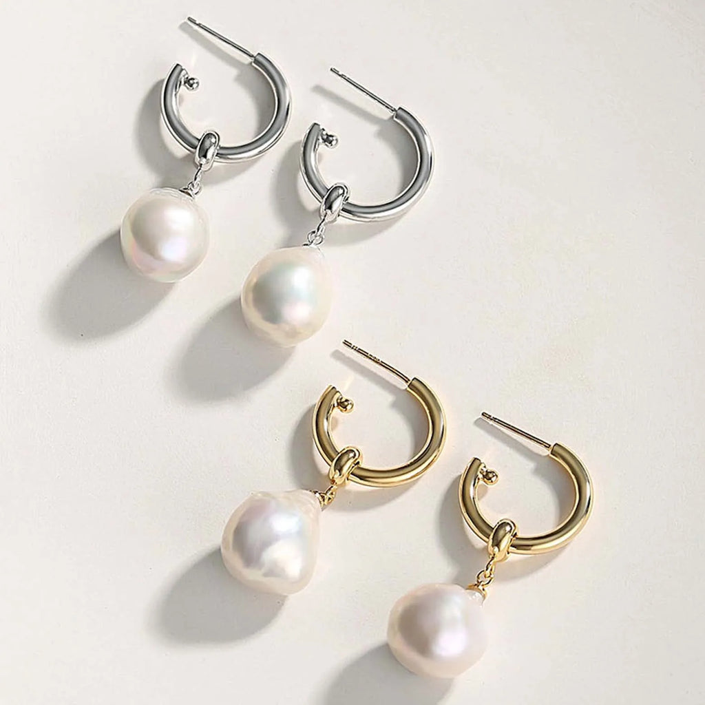 The image features two pairs of hoop earrings, each with a pearl pendant. On the left, there is a pair of silver hoop earrings with a classic latch-back closure, from which a single round white pearl is suspended on each, their iridescence giving off a soft glow. On the right, there is a pair of gold hoop earrings designed with a thicker circumference and a smooth finish, also featuring a round white pearl pendant hanging from each hoop.