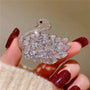 Diamond swan brooch held between fingers with red nail polish on a neutral background