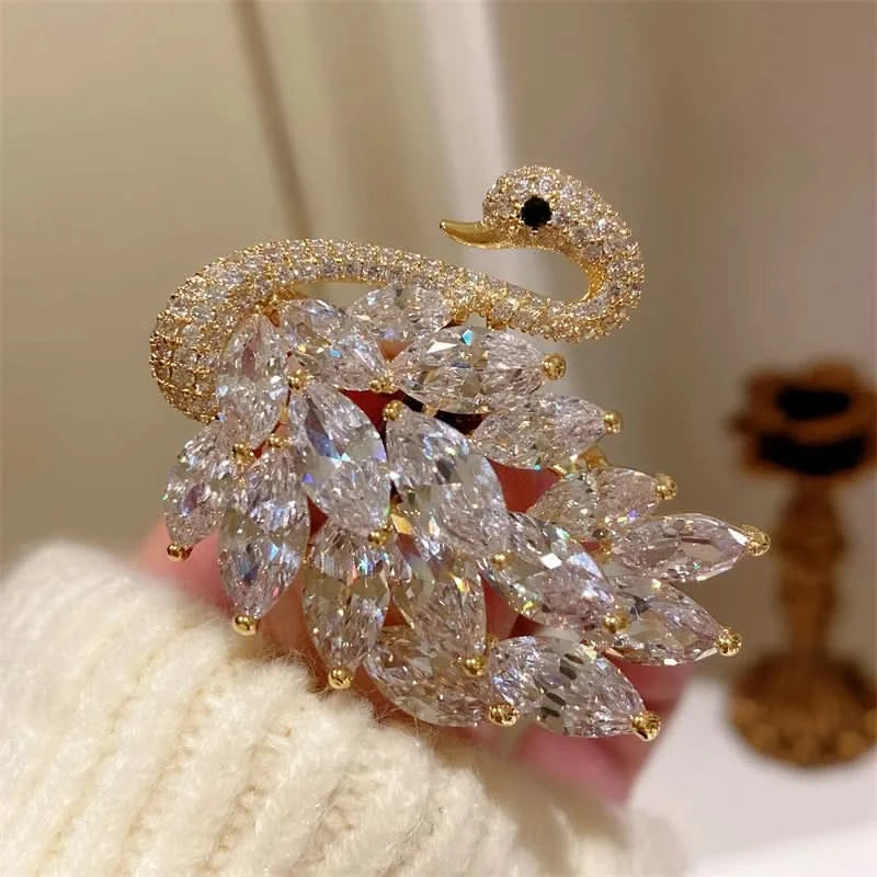Gold and crystal swan brooch held by a person wearing a white sweater.