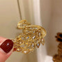 Gold brooch with intricate design held by a hand against a neutral background