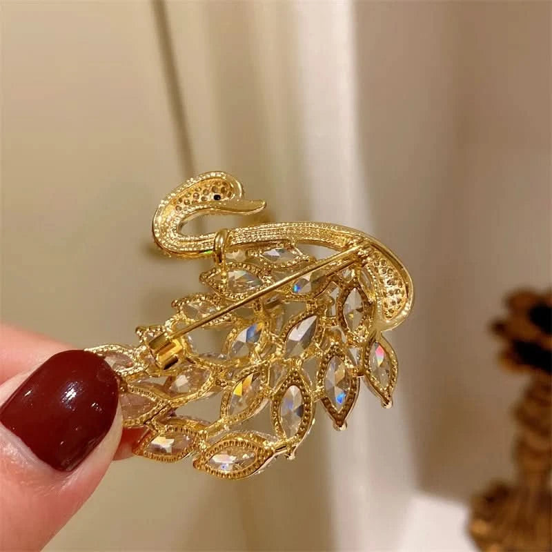 Gold brooch with intricate design held by a hand against a neutral background
