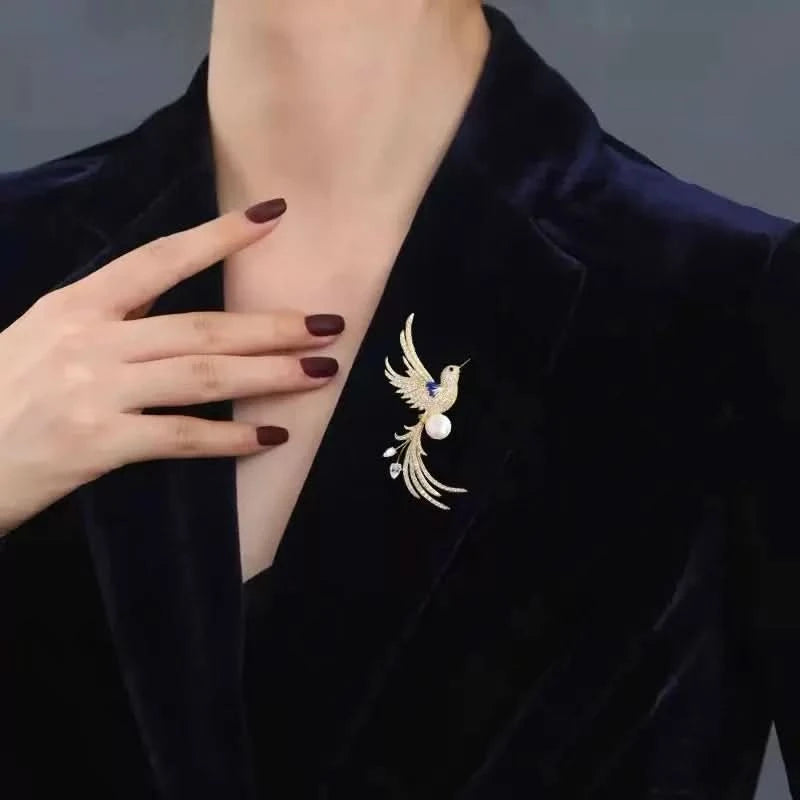 Gold-tone crystal bird brooch with pearl accent worn on a navy velvet blazer