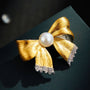 Close-up of two-tone brushed gold bow brooch with freshwater pearl and crystal-set ribbon ends on a dark background