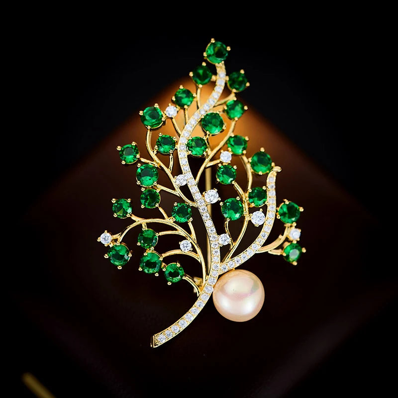 Close-up of green faceted crystals arranged along curved gold-tone branches with pearl accent