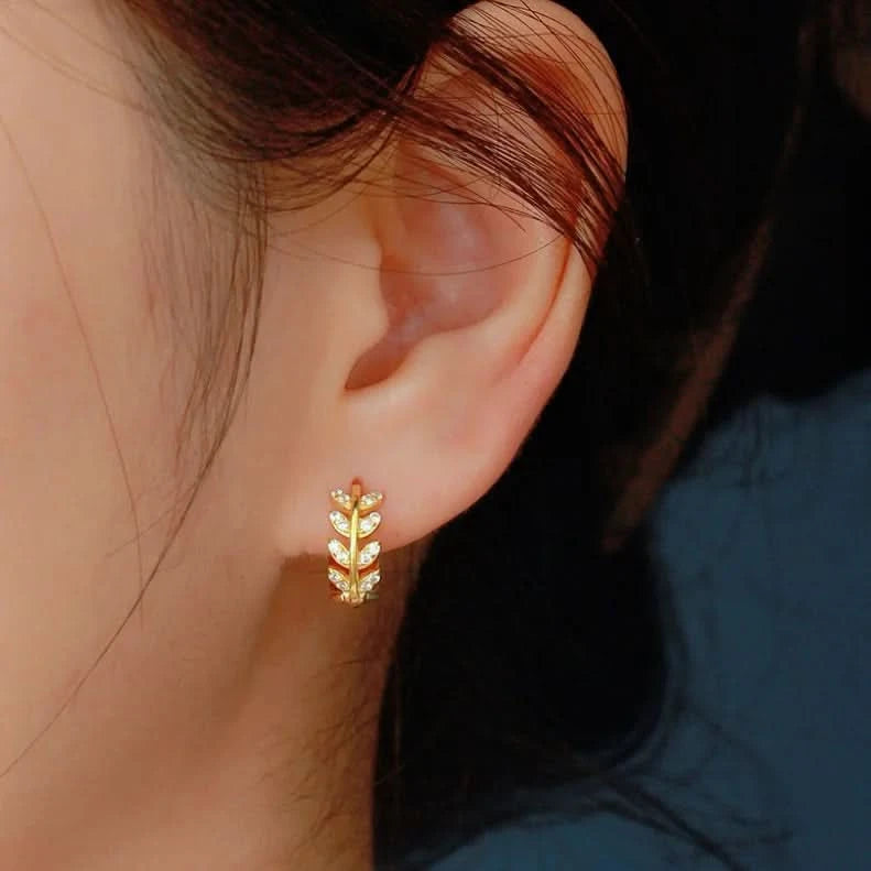 Gold leaf-shaped earring worn by a person with a blurred background