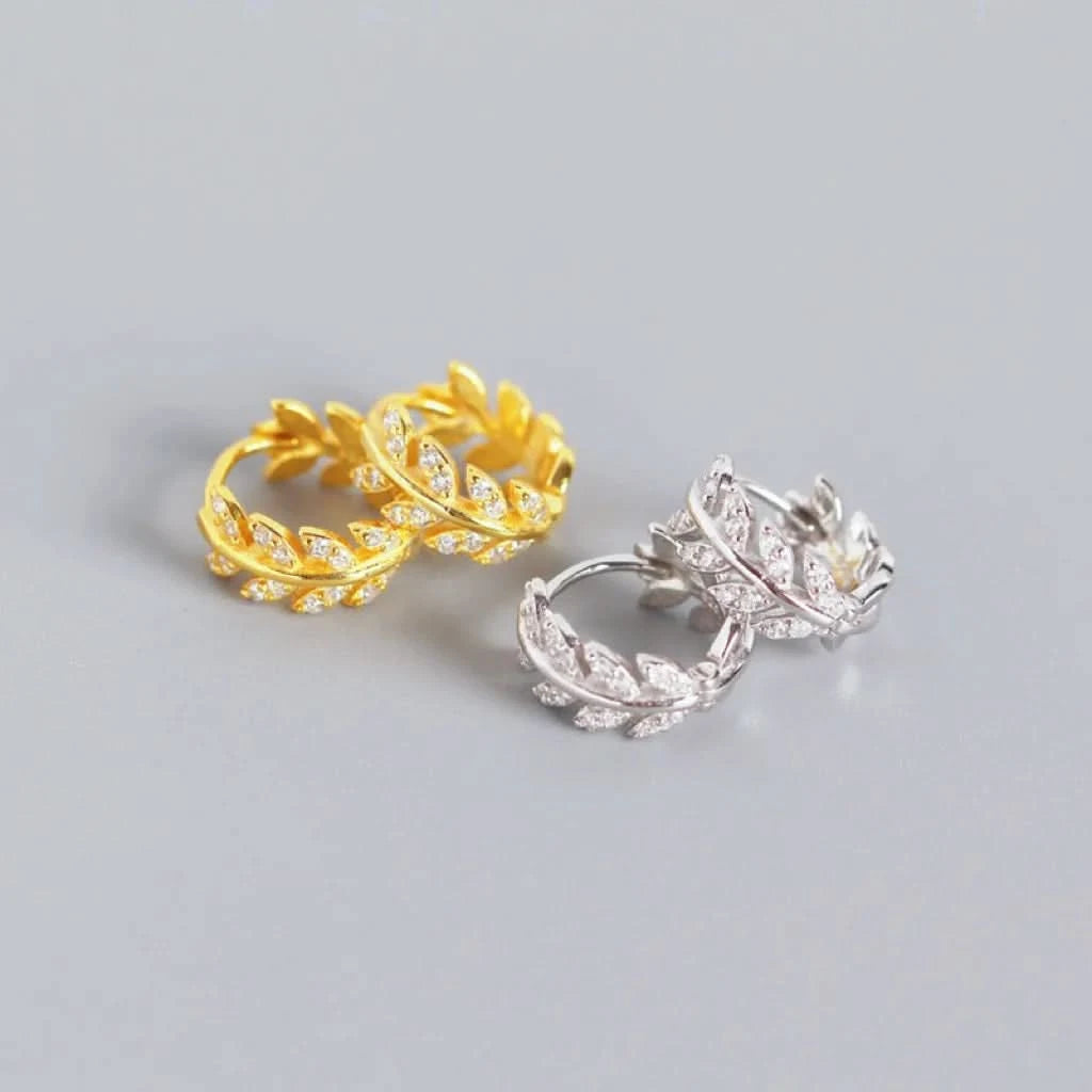 Gold and silver leaf-shaped earrings on a gray background