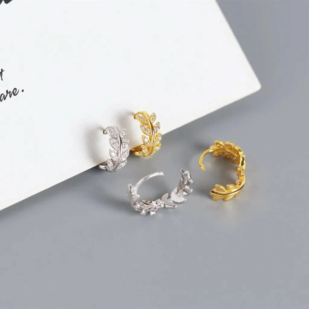 Two pairs of gold and silver leaf-shaped earrings on a gray surface.