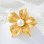 Freshwater pearl brushed gold flower brooch and pendant styled on a white textured background