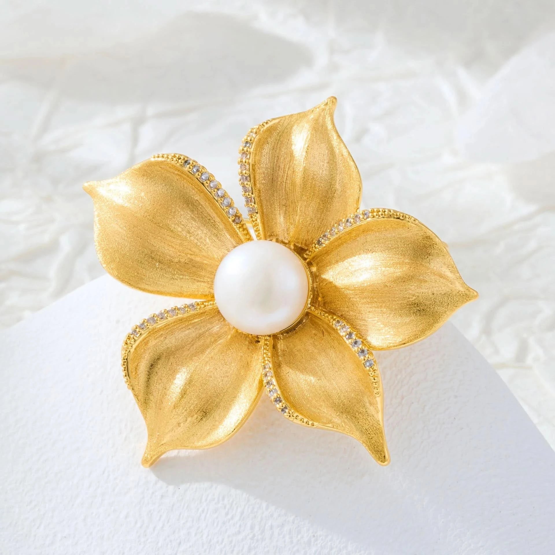Freshwater pearl brushed gold flower brooch and pendant styled on a white textured background