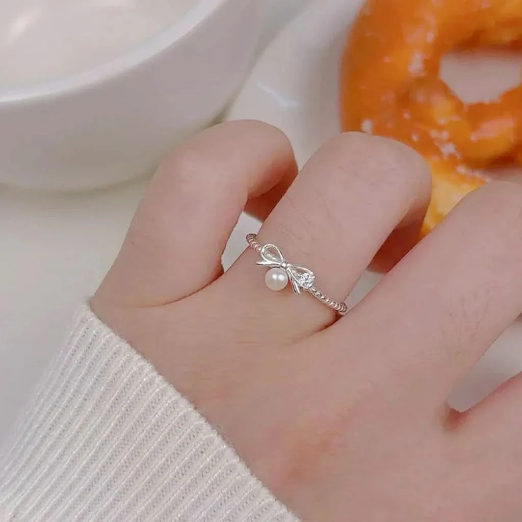 Hand wearing a silver ring with a pearl and bow design