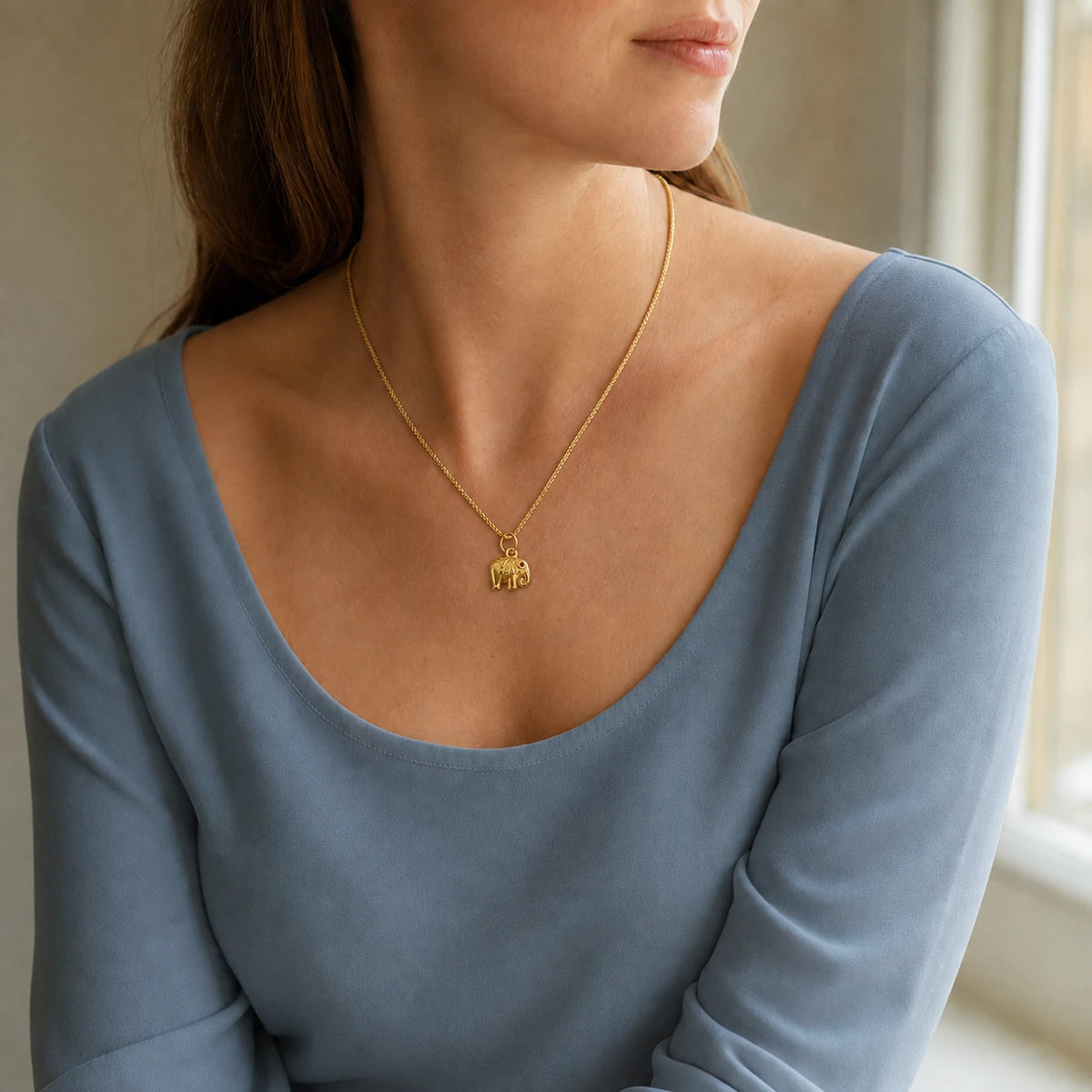 Model wearing gold-tone elephant pendant necklace with red stone accent