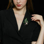 Green crystal branch and pearl brooch worn on a black blazer with a V-neckline