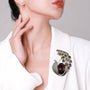 Vintage peacock feather crystal brooch worn on a white blazer