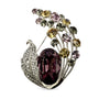 Vintage peacock feather crystal brooch with deep purple centre stone on white background